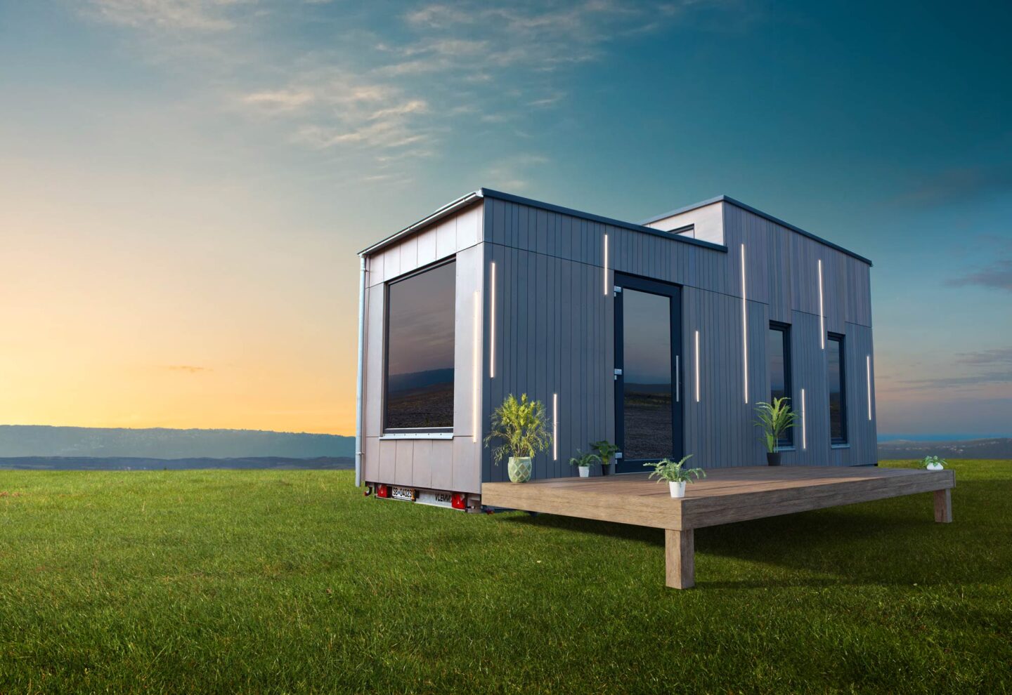 Ein modernes kleines Haus mit großen Fenstern steht bei Sonnenuntergang auf einer Wiese - ein perfektes Beispiel für Saarland Marketing. Davor erstreckt sich eine Holzterrasse mit Topfpflanzen, und der Himmel ist meist klar mit ein paar Wolken.