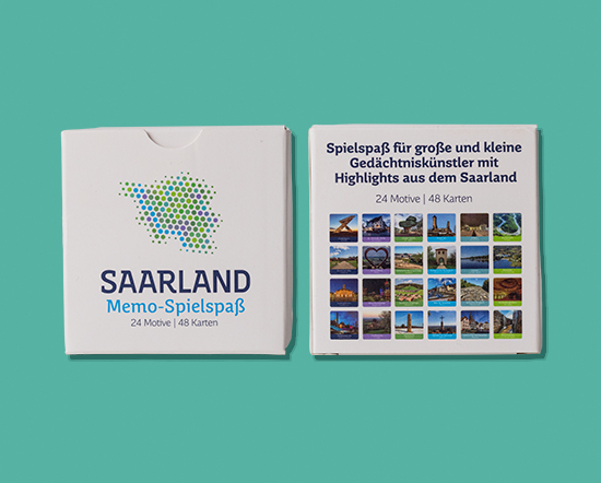 Zwei saarländische Kartenspielschachteln auf türkisfarbenem Hintergrund; die linke Schachtel zeigt eine gepunktete Karte und den Titel, während die rechte Schachtel die Spieldetails und Fotos saarländischer Wahrzeichen zeigt.